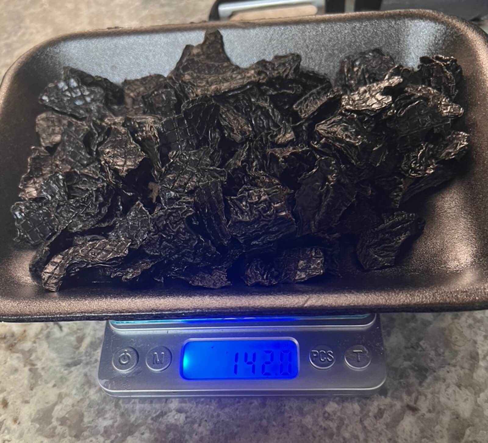 Finished dehydrated beef liver treats weighed on a digital scale showing 142 grams, about a third of the raw weight