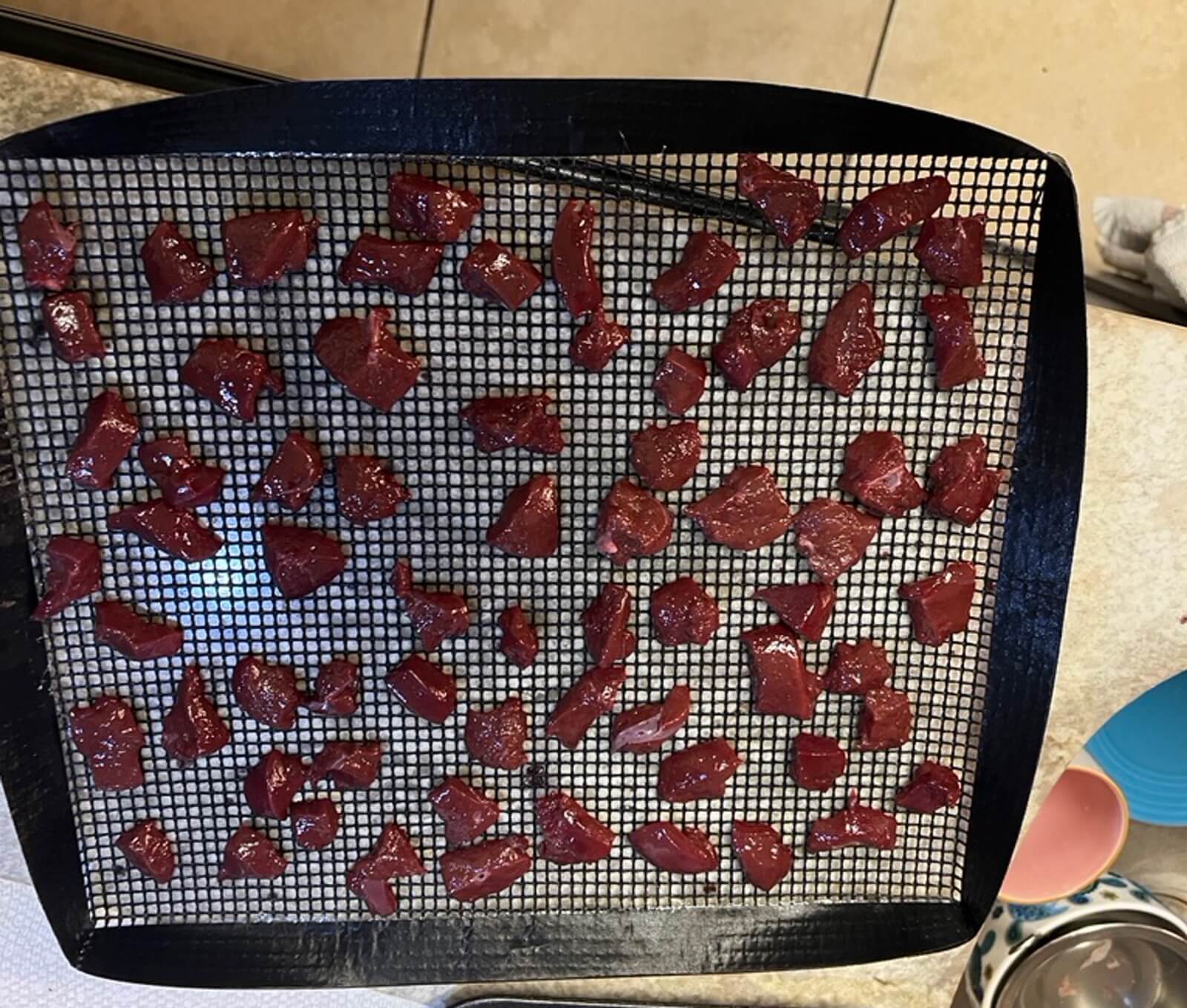 Beef liver cubes spread evenly on a wire dehydrating rack before going into the oven